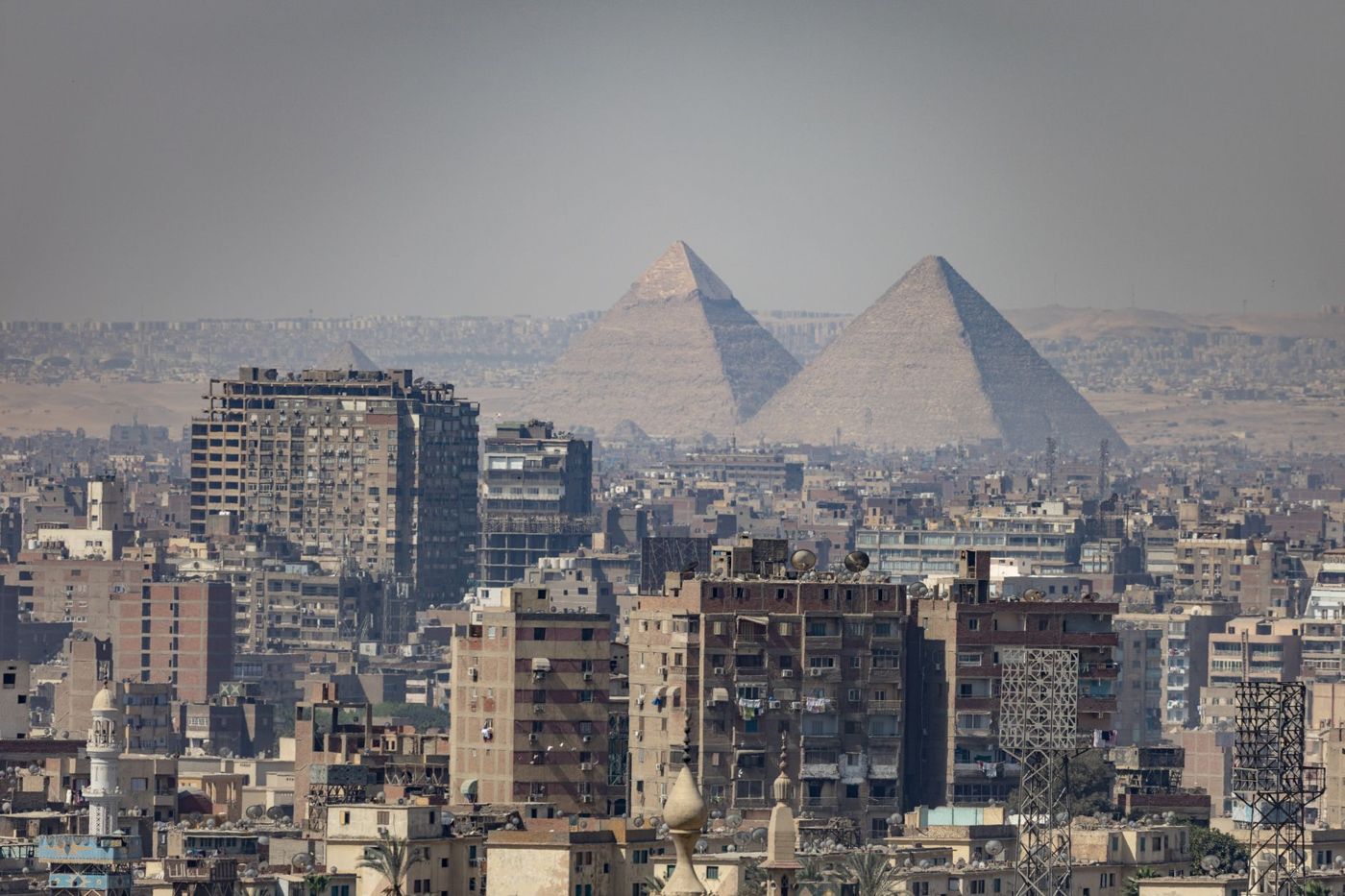 The three Pyramids of Giza in the afternoon sun, with the outskirts of Cairo in the background