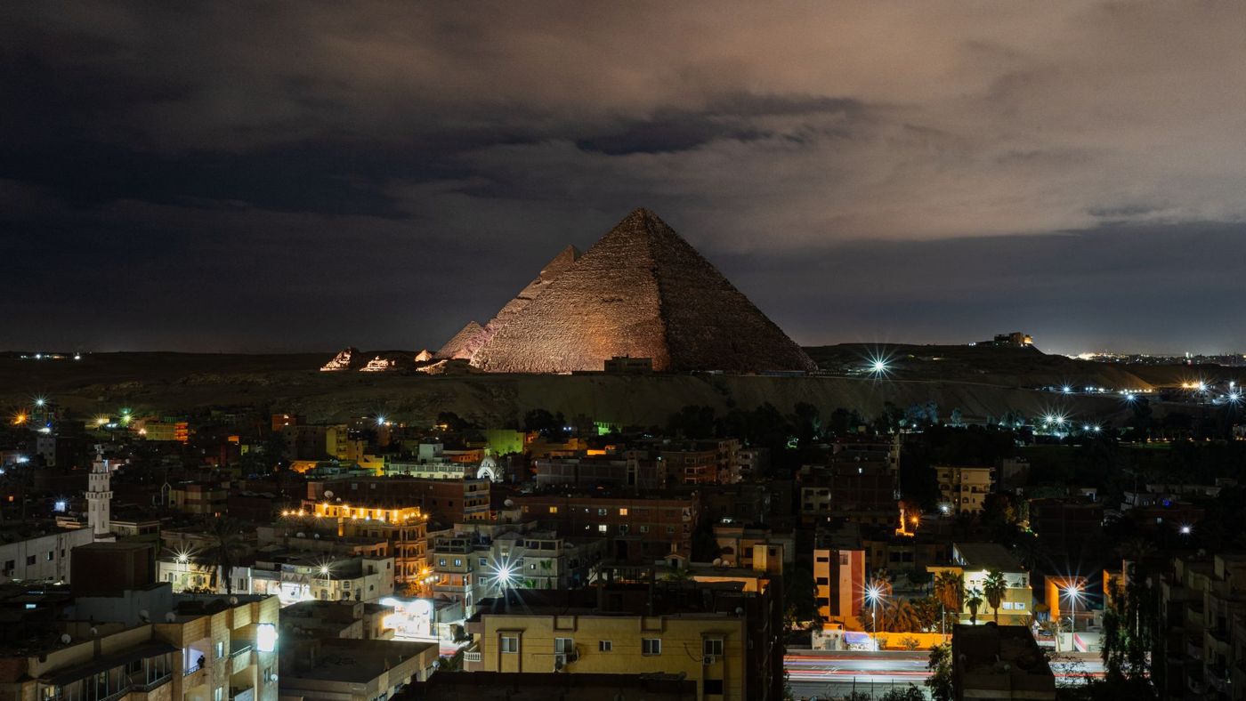 As pirâmides de Gizé iluminadas após o anoitecer, vistas de um terraço