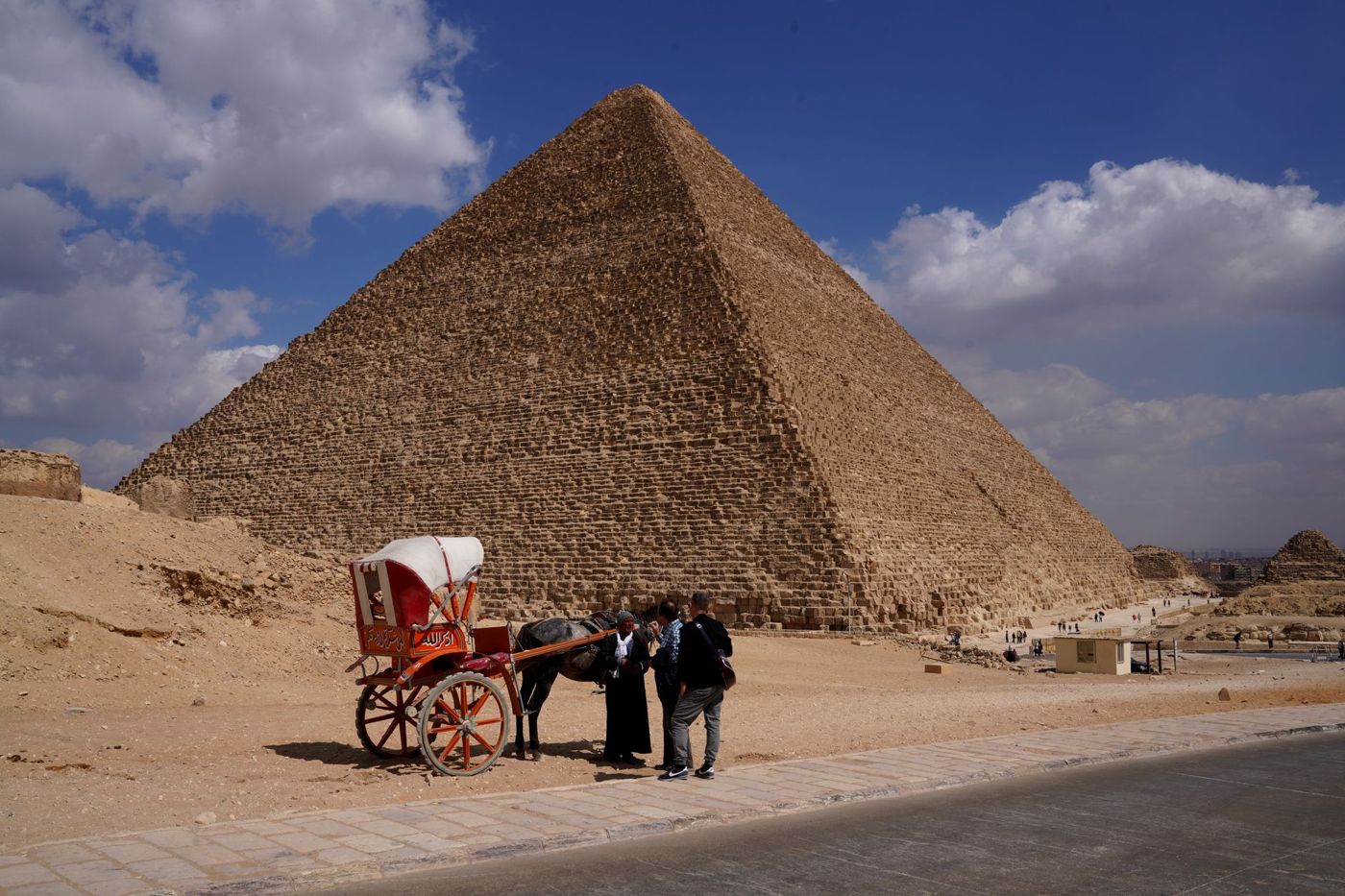 Des visiteurs se tiennent au pied de la plus grande pyramide à côté de blocs de pierre à hauteur d'homme
