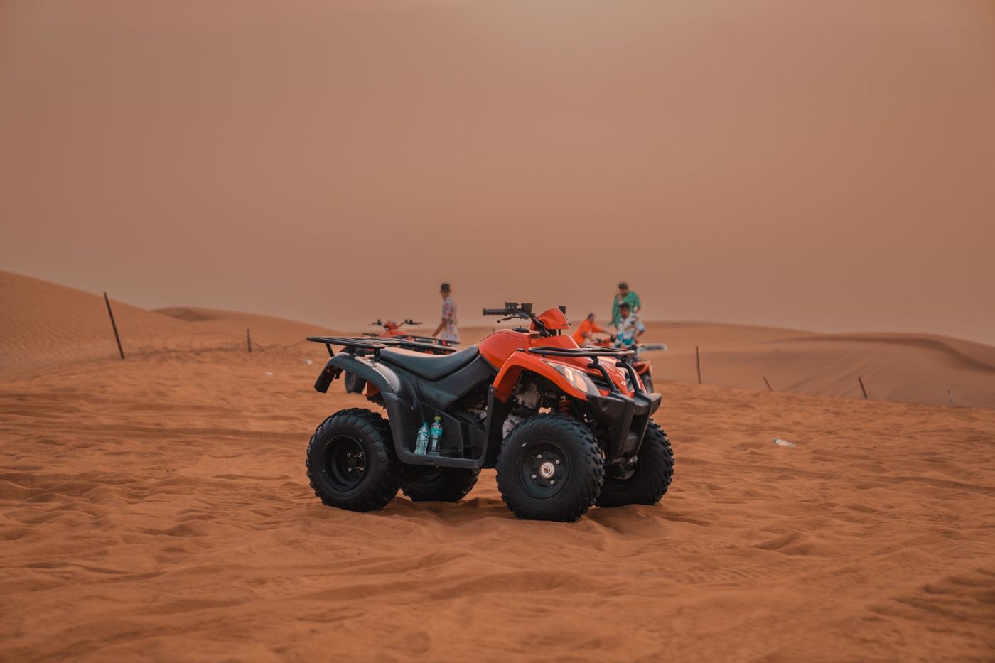 Fila de quads aparcados al borde de una duna de arena, conductores con cascos