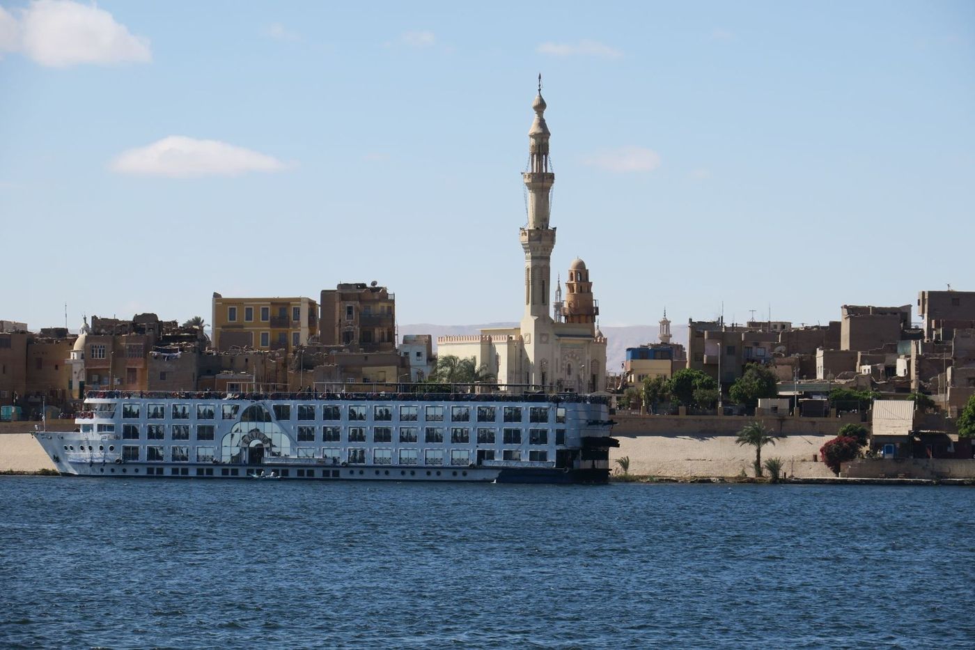 White Nile cruise ship on the river near Aswan, with the city and a minaret behind it